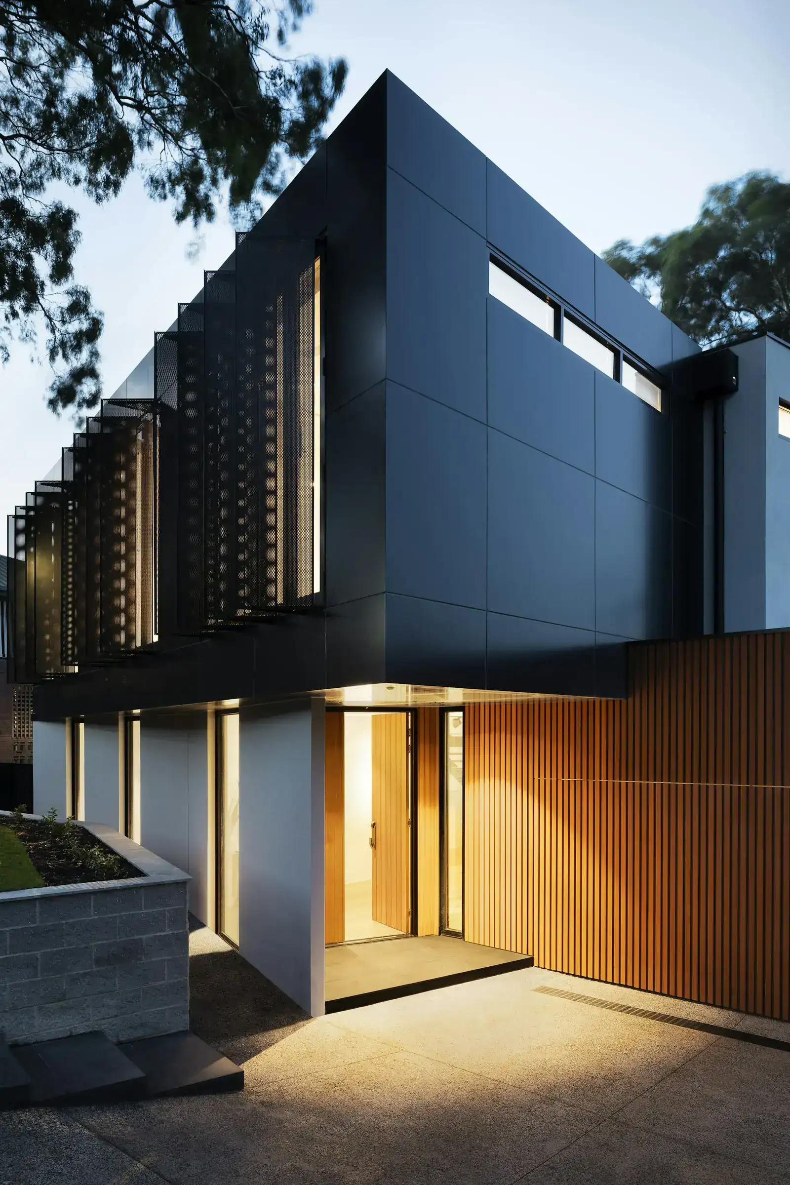 Modern house at dusk with a warmly lit entry and timber slats